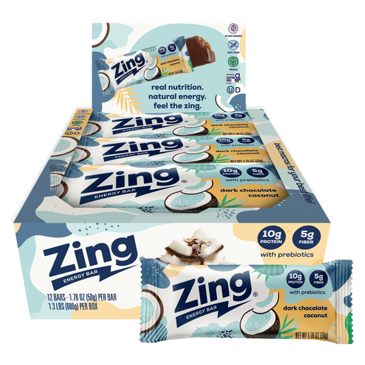 A box of Zing Energy Bar snack sticks with two individual bars displayed in front on a plain white background. The packaging features light blue, white, and yellow graphics with coconut illustrations and text indicating dark chocolate coconut flavor and prebiotics.