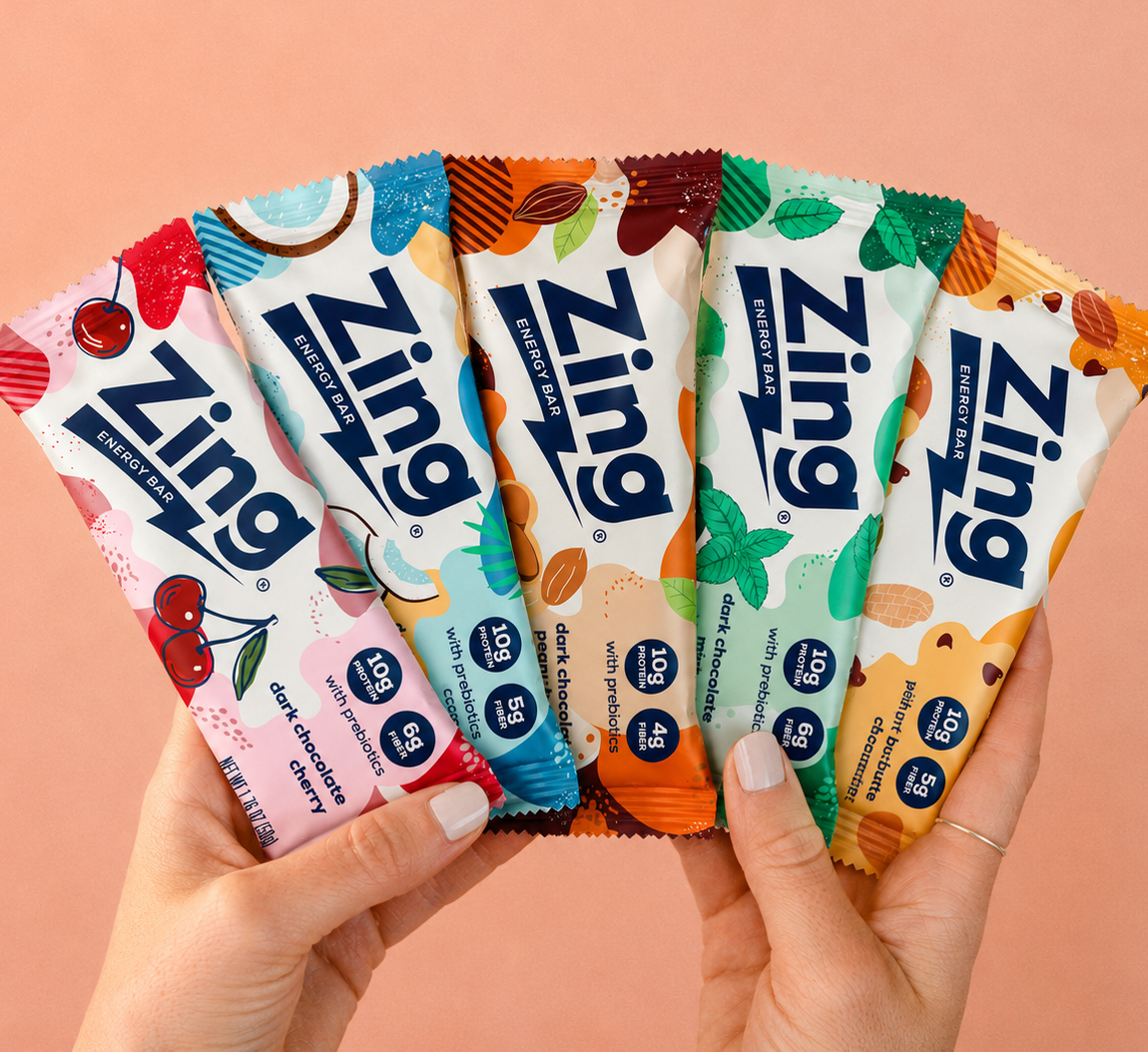 Hands holding five Zing Bars energy bar flavors including Dark Chocolate Cherry, Coconut, Mint, and Peanut Butter Chocolate Chip